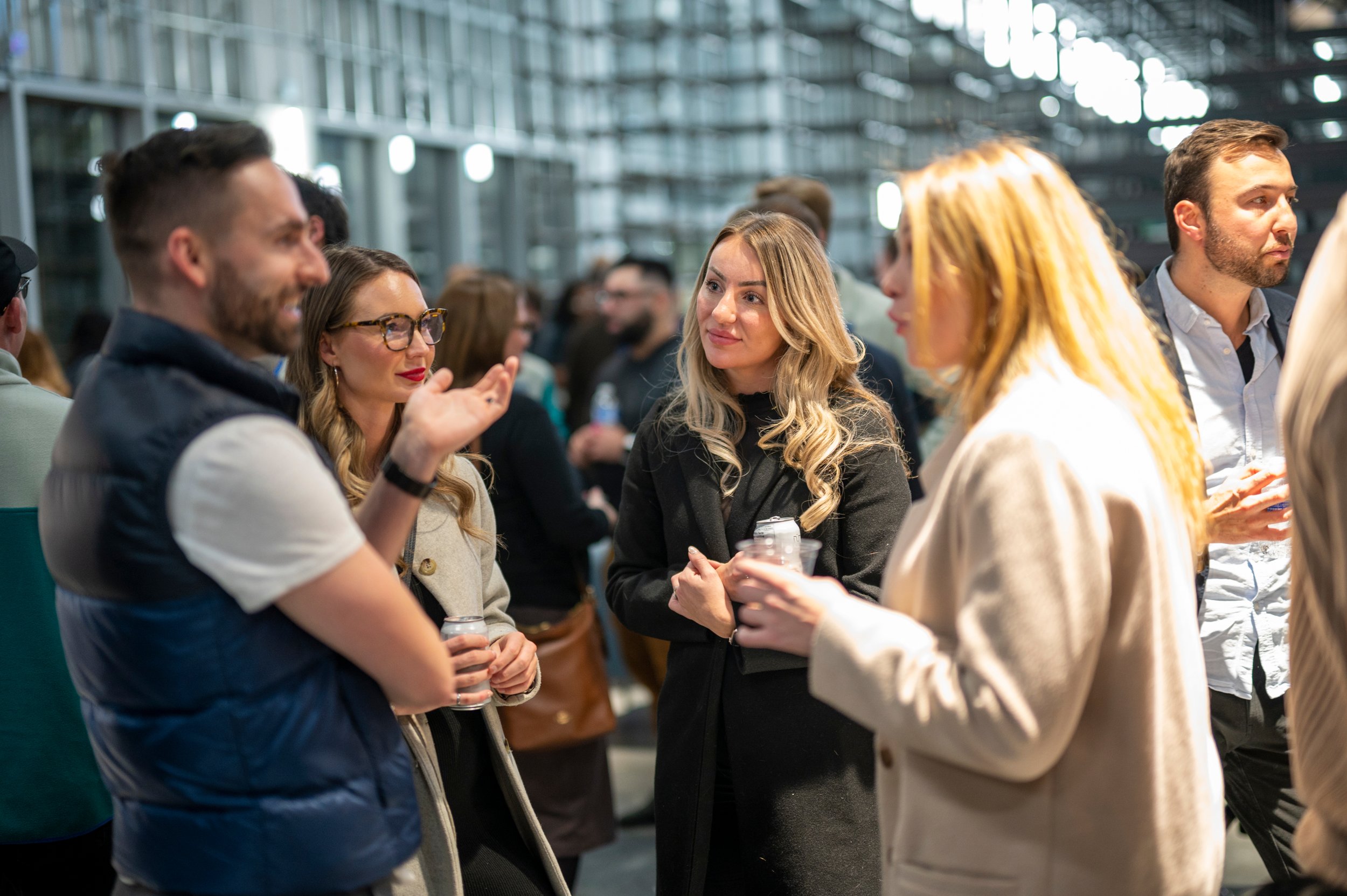 A group of community members socializing at an indoor event, some holding drinks and engaged in conversation.